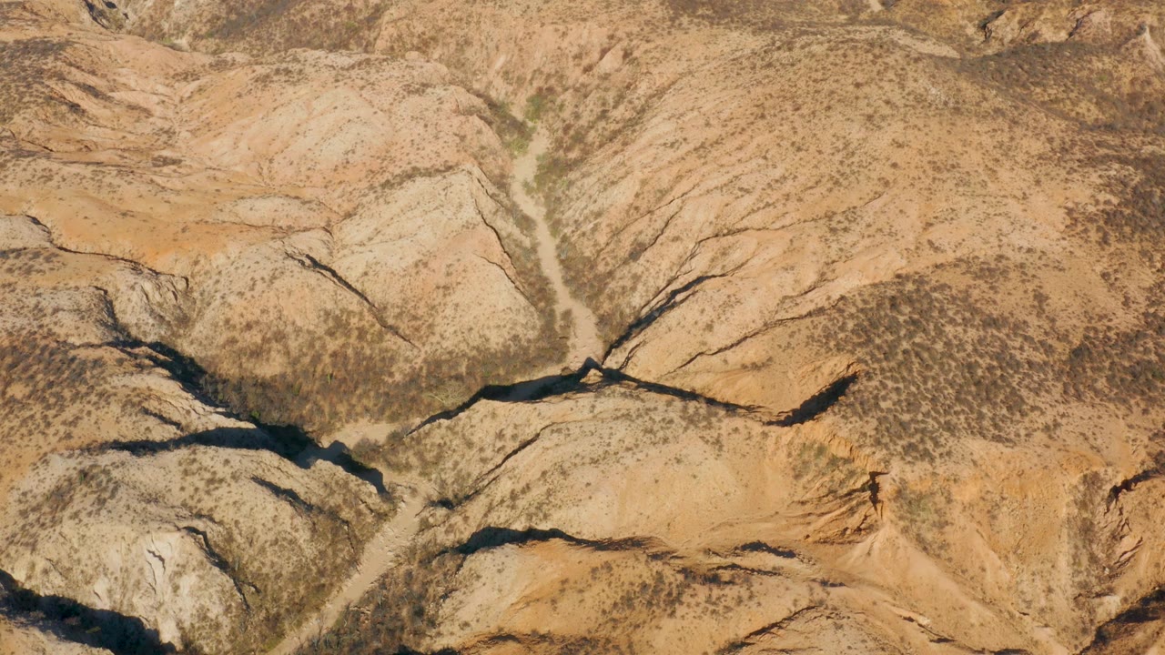 Aerial view in Cabo Pulmo with rounded tan ridges, dark ravine cuts, scrub patches, and no visible people or structures.