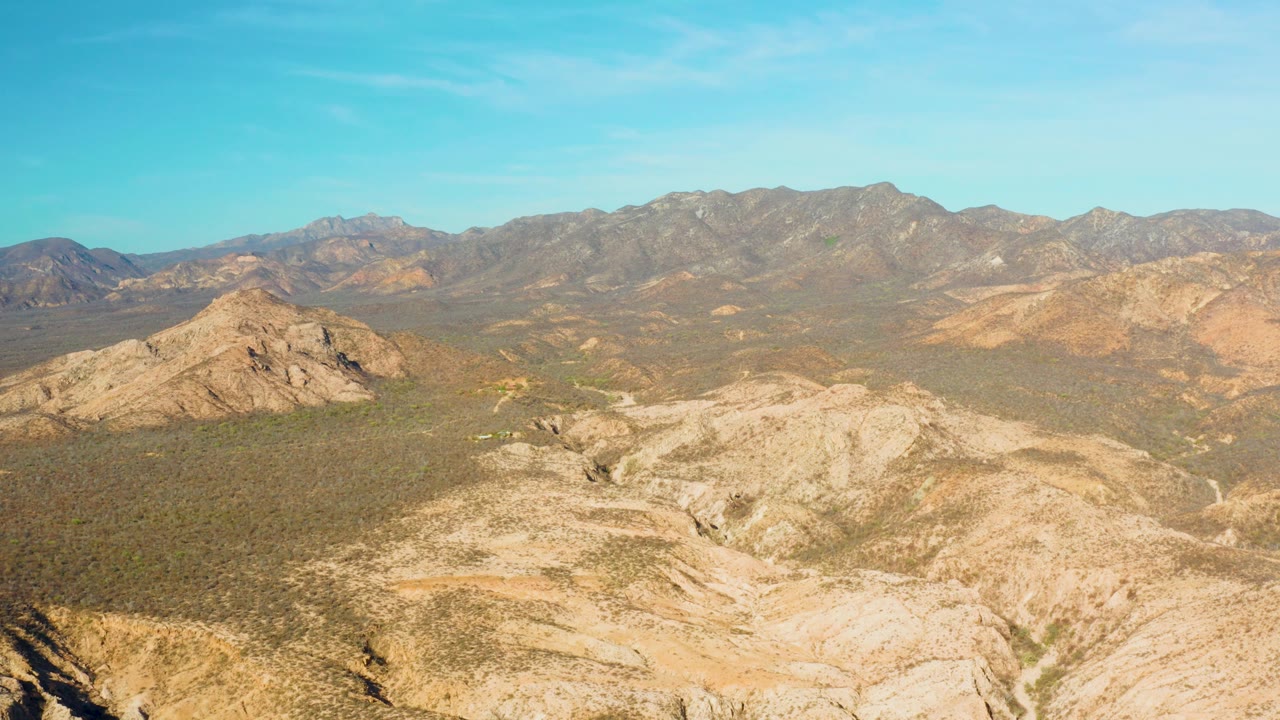 Wide aerial view of rocky desert ridges and distant mountains under blue sky.