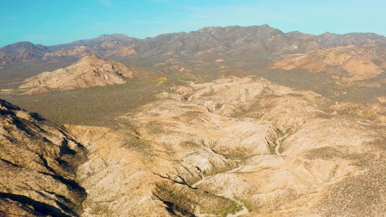 Dry mountain basin with tan ridges, dark foreground shadow, and blue sky.