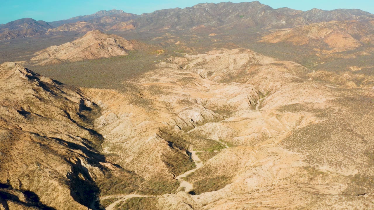 At mid-clip, the Cabo Pulmo aerial composition shows a shadowed rocky ridge on the left, winding dry channels through the center, and mountains lining the horizon, with no visible people.