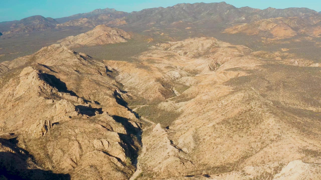 Sunlit desert ridges with shadowed gullies and mountains beyond.
