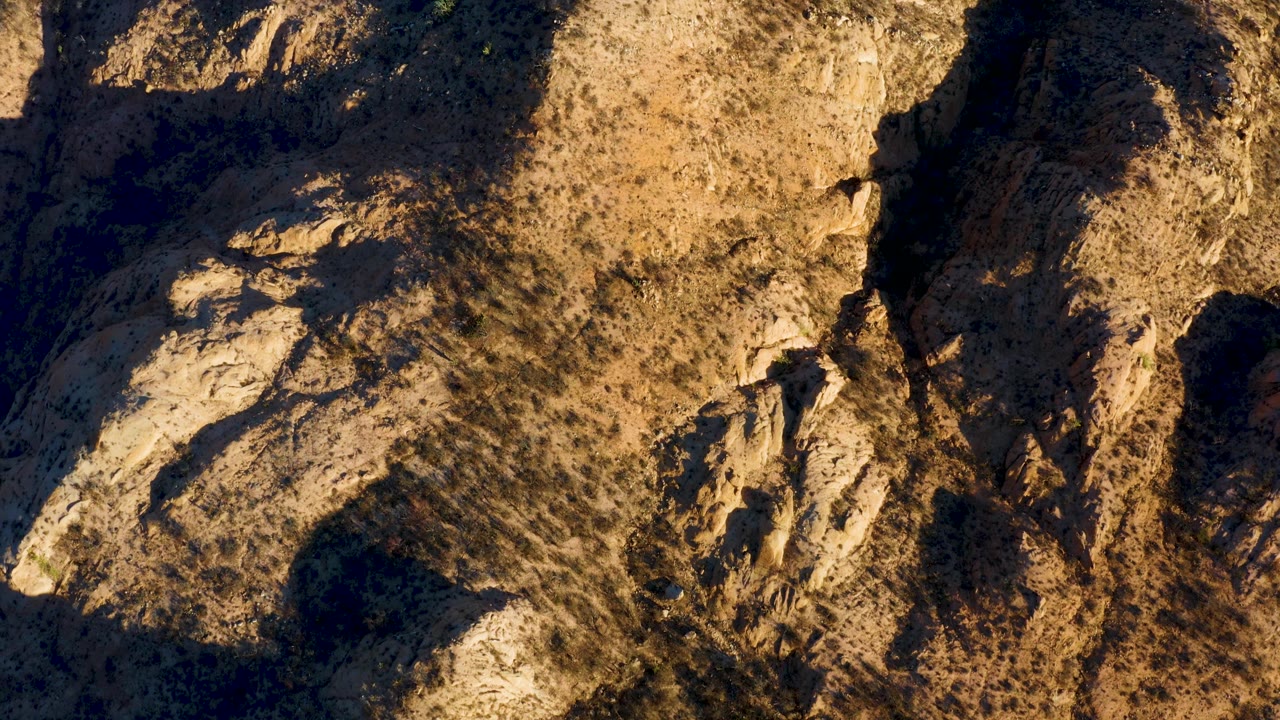 Rocky arid slope with long shadows across scrub