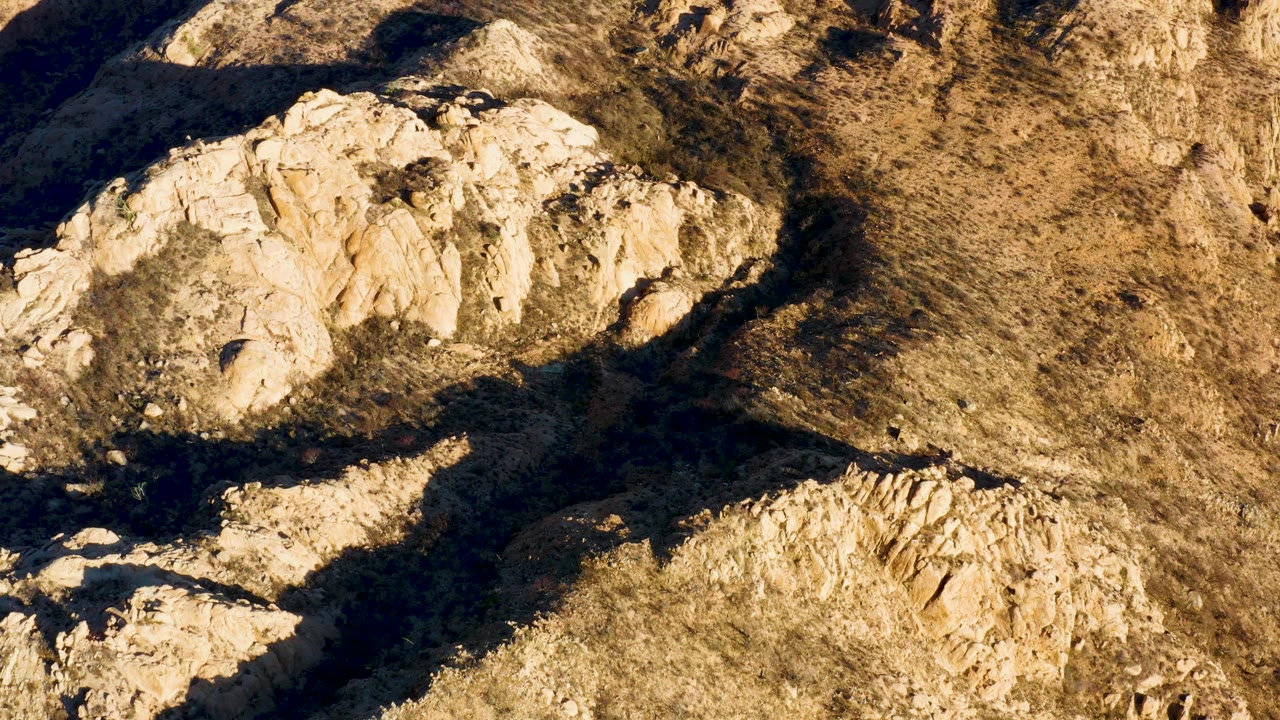 Aerial view in Cabo Pulmo showing sunlit beige rock ledges beside darker shadowed channels and rough brown desert surface, no visible people.