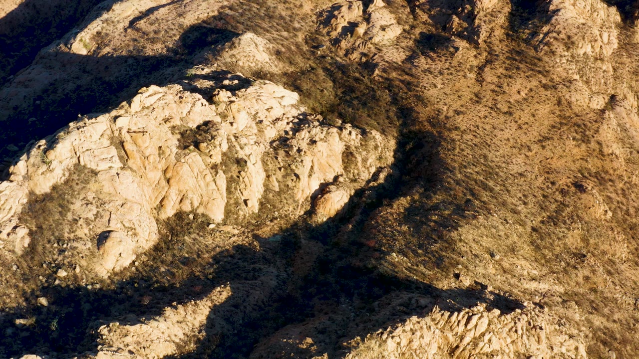 Downward aerial view over Cabo Pulmo terrain, with a bright beige rock mass across the left half and a broad dark shadow cutting through the lower center, no visible people.