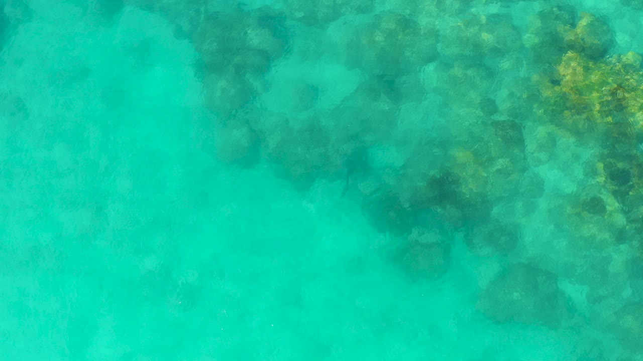 Shallow blue-green water reveals a larger cluster of underwater rocks and coral in Cabo Pulmo, with no visible people.