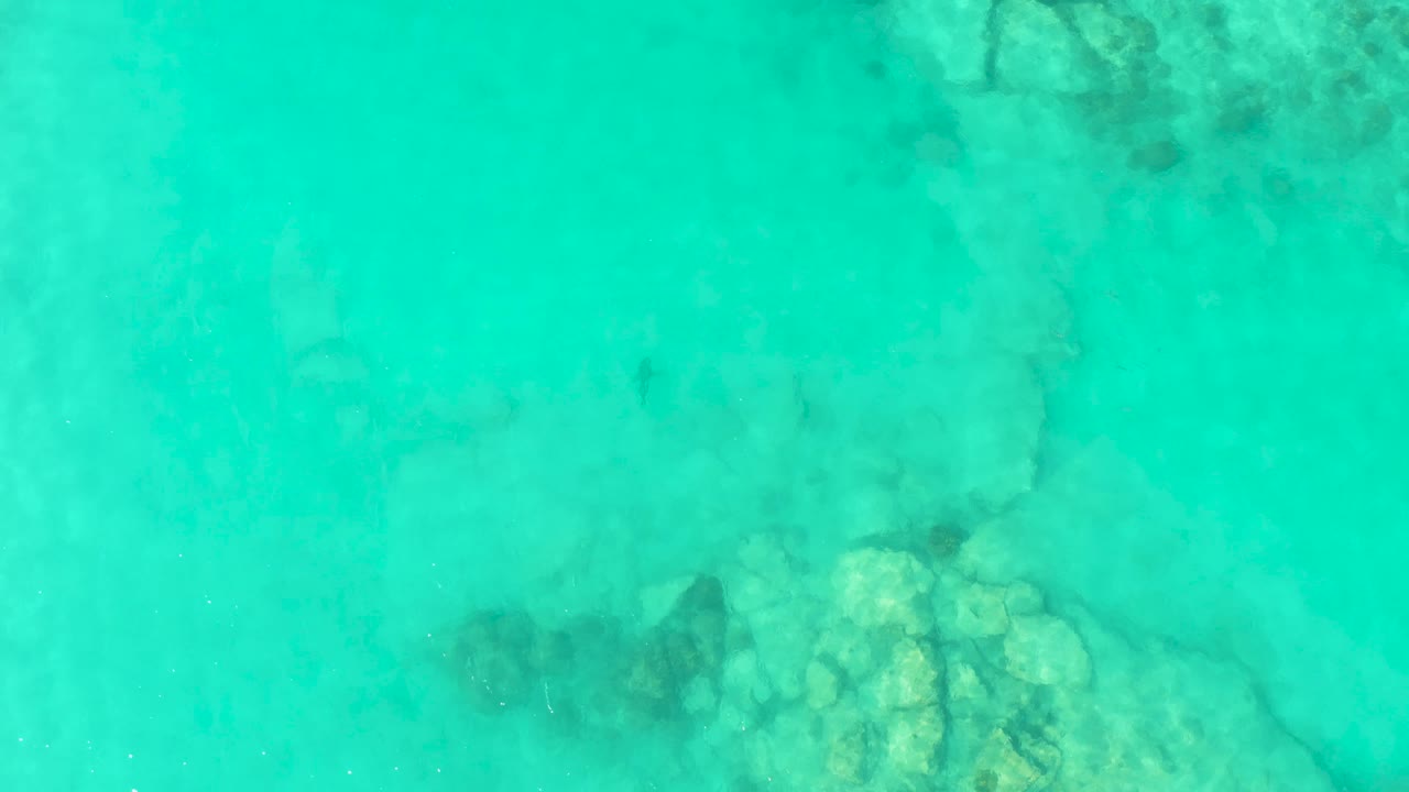 Pale underwater rocks and darker seabed marks are visible through turquoise water in Cabo Pulmo, Baja California Sur, with no visible people.