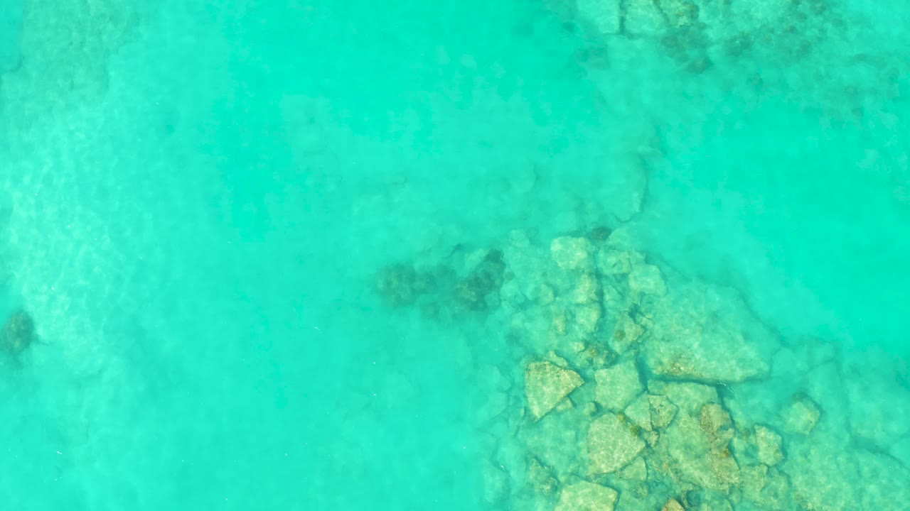 Overhead view of clear turquoise water in Cabo Pulmo with a cluster of submerged rocks near the lower center and no visible people.