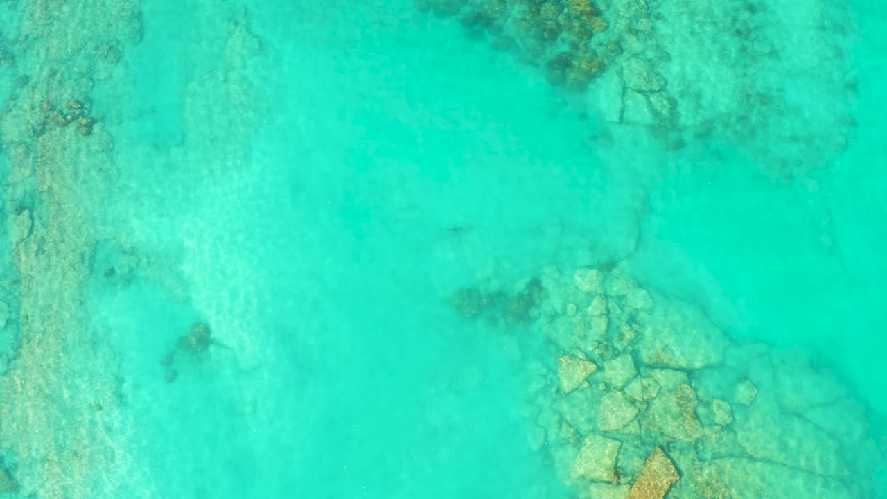 Clear Cabo Pulmo water shows a broad pale bottom and a cluster of submerged rocks along the lower right edge, with no visible people.