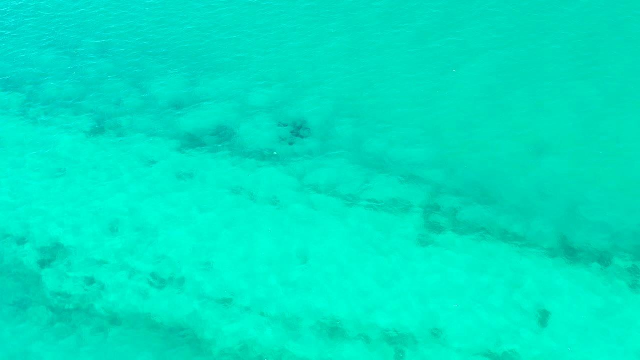 Turquoise shallow water over a sandy seabed with dark patches.
