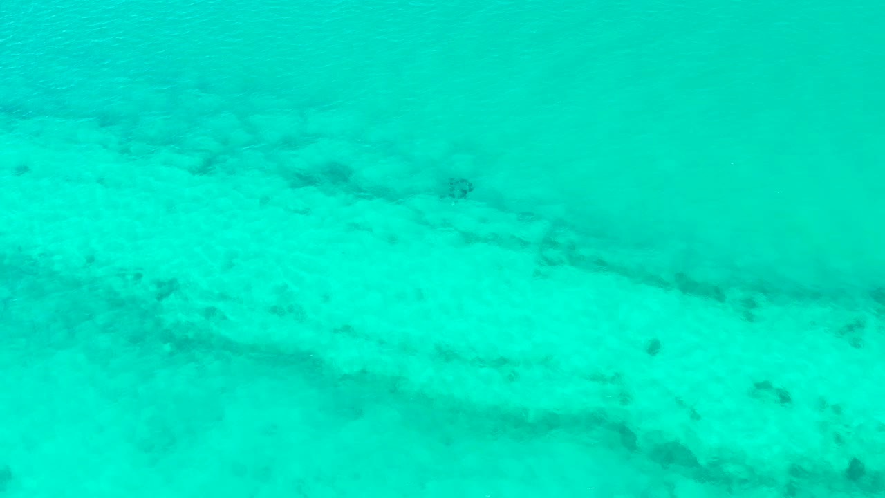 Mid-clip frame of calm turquoise water over a pale sandy seabed in Cabo Pulmo, with darker underwater bands near the lower edge and no visible people.