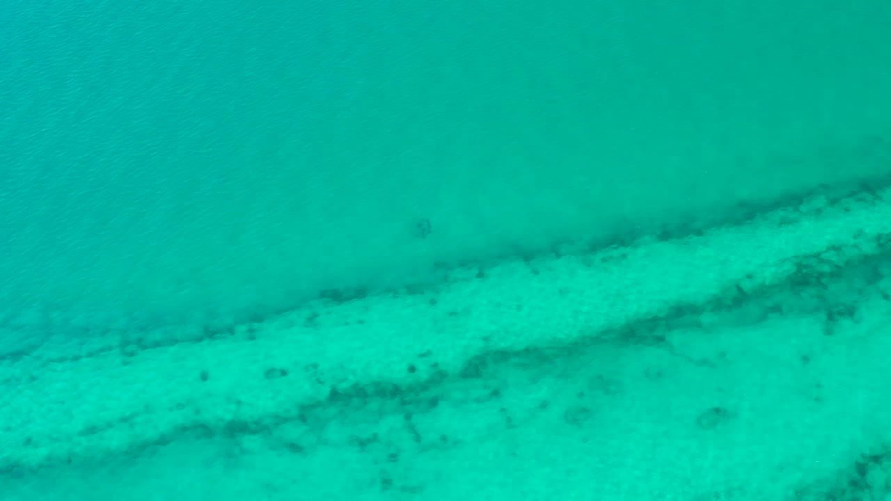 At two seconds, the Cabo Pulmo aerial frame keeps the water surface full-screen while darker coral-like patches appear beneath the blue-green shallows, with no visible people.