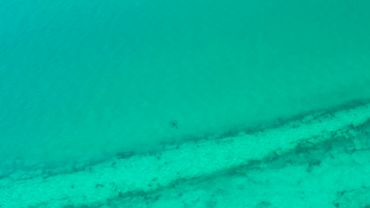 Mid-clip Cabo Pulmo frame where bright sand and darker underwater streaks remain visible through the turquoise water, with no visible people.
