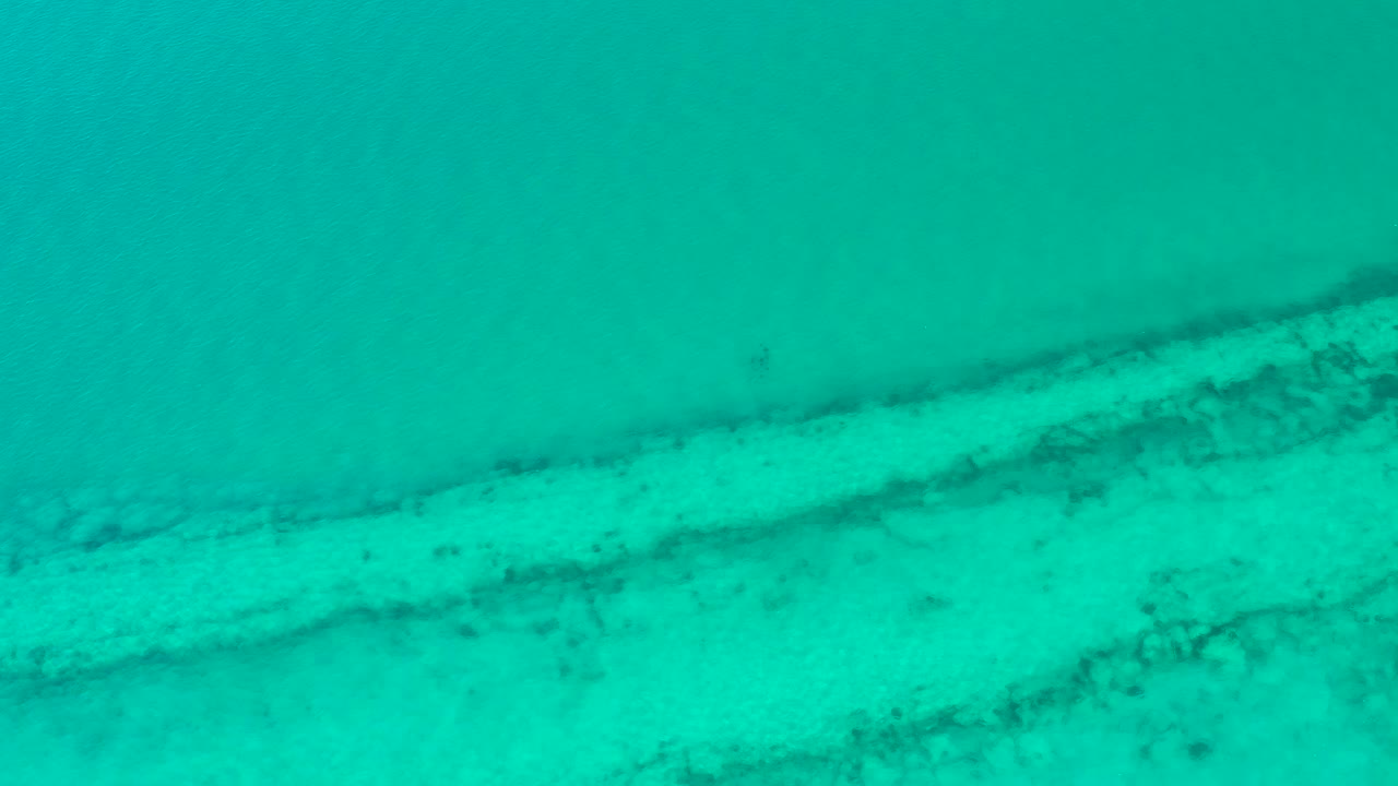Turquoise shallow ocean over sand and darker reef bands.