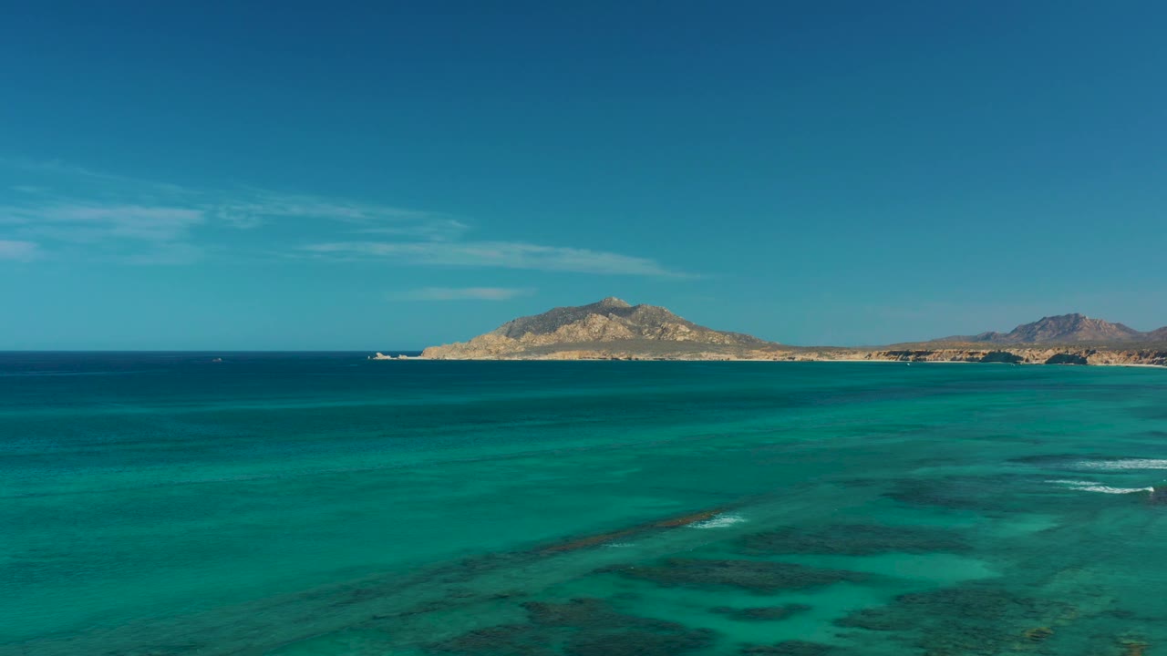 Open turquoise ocean with low island and blue sky.