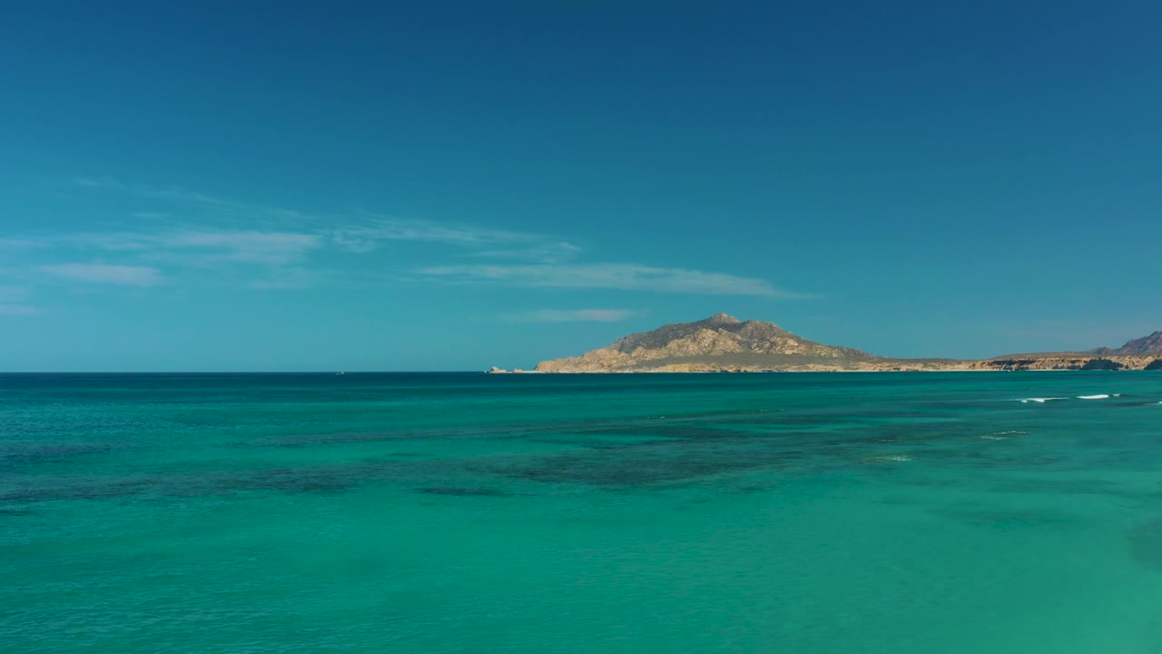 Blue-green sea and darker underwater patches lead toward a low island horizon in Cabo Pulmo, with no visible people.