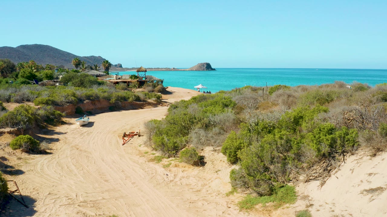 Sandy beach path with scrub bushes and turquoise ocean beyond.