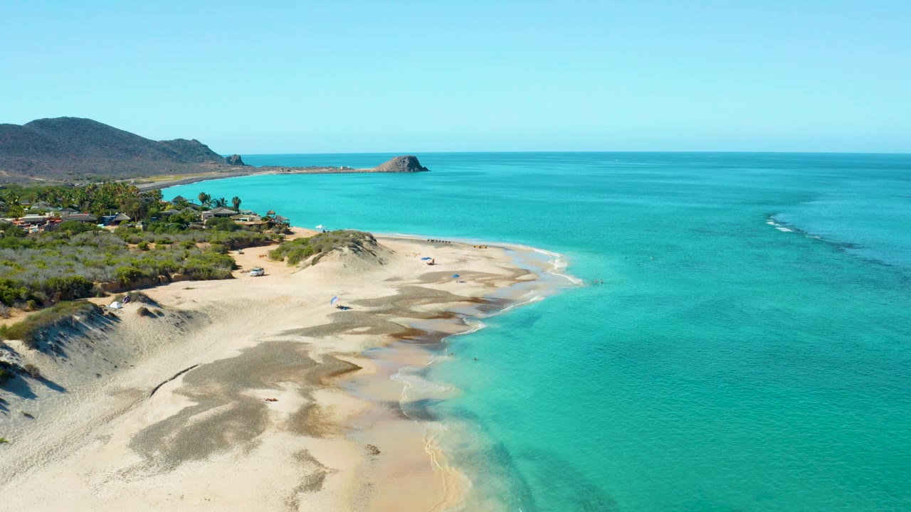 Aerial beach point with turquoise water and coastal vegetation.