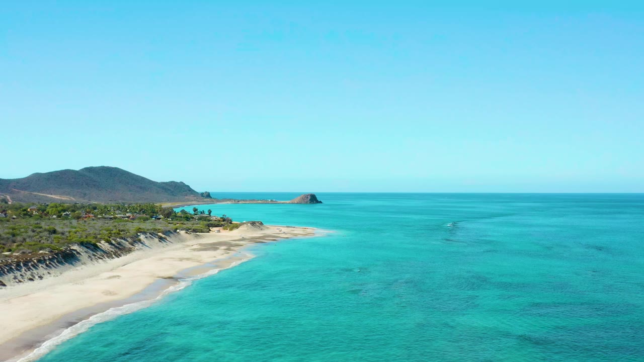 At 0:01, the Cabo Pulmo beach remains along the left edge while clear turquoise water fills the foreground and midground, with no visible people on the sand or in the water.