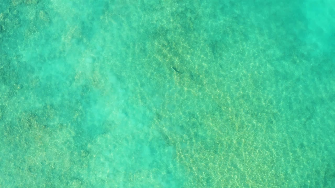 Turquoise shallow water over a sandy seabed with ripple light patterns.