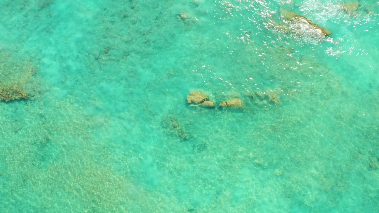 Clear shallow water with coral patches and small rocks below the surface.