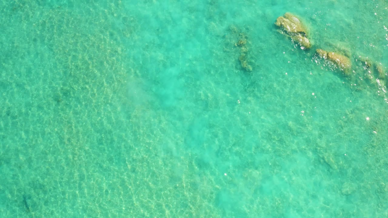 Overhead view of clear turquoise water in Cabo Pulmo with submerged rock formations near the upper right and no visible people.
