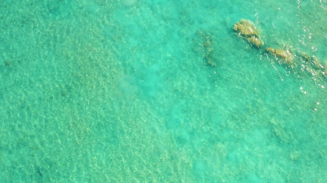 Straight-down view of Cabo Pulmo turquoise water with scattered underwater rock shapes near the upper right edge and no visible people.