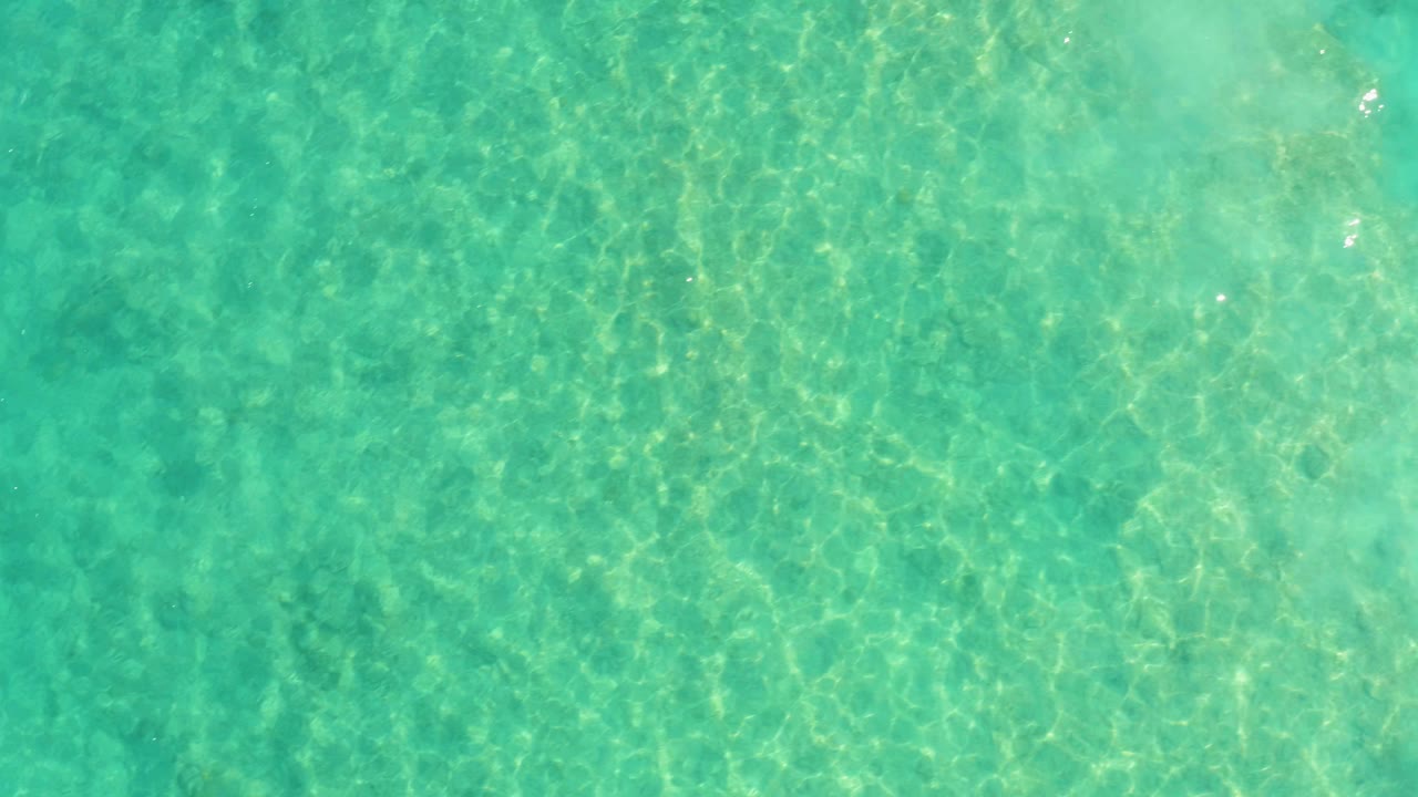 Top-down view of clear turquoise water in Cabo Pulmo with faint sandy seabed texture and no visible people.