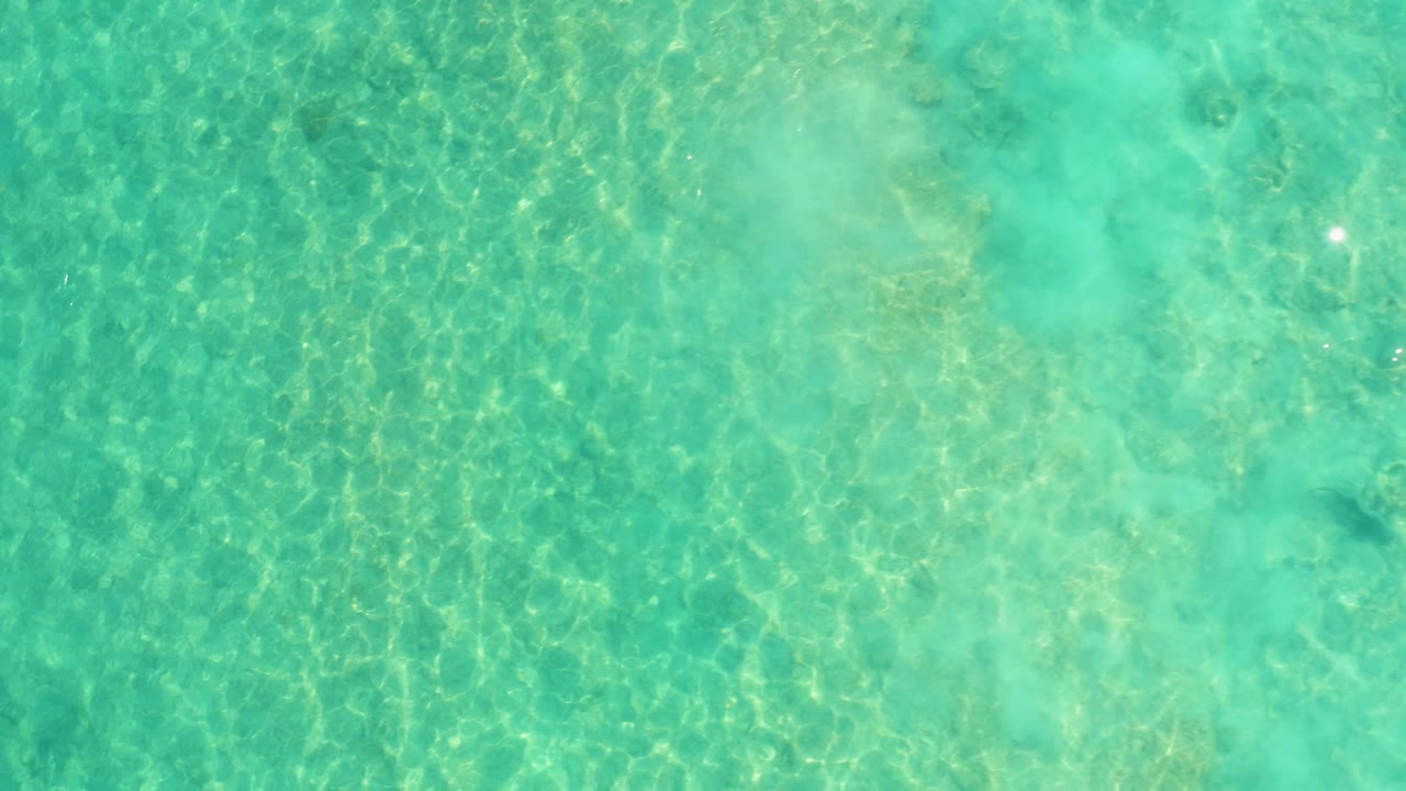 A top-down Cabo Pulmo water frame shows pale seabed shapes beneath turquoise ripples, with no visible people or boats.