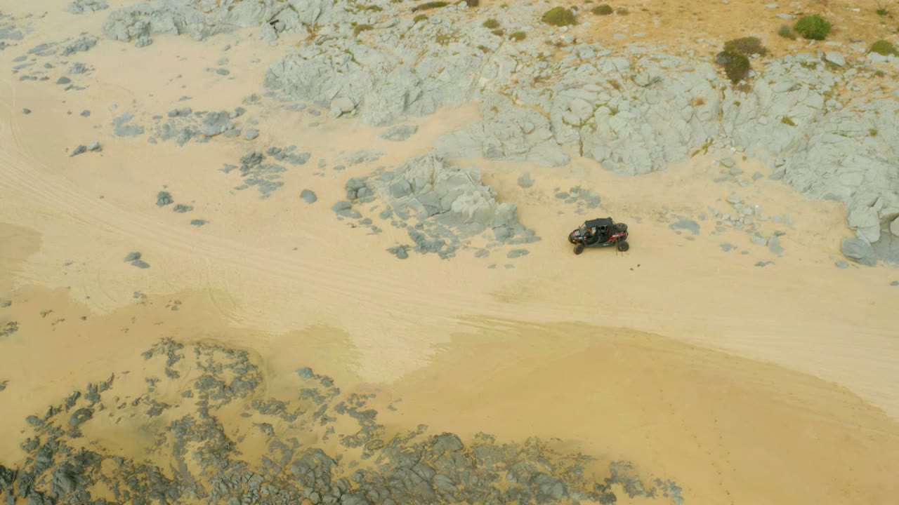Dark off-road vehicle crossing sandy ground below rocky patches.