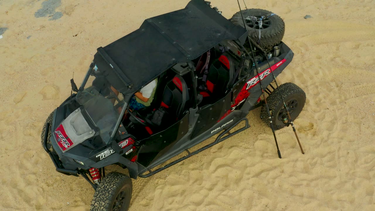 High-angle frame of the off-road buggy in Laguna Beach Los Cabos, Baja California Sur, showing the rear spare tire, whip antennas, red side graphics, and no visible people.