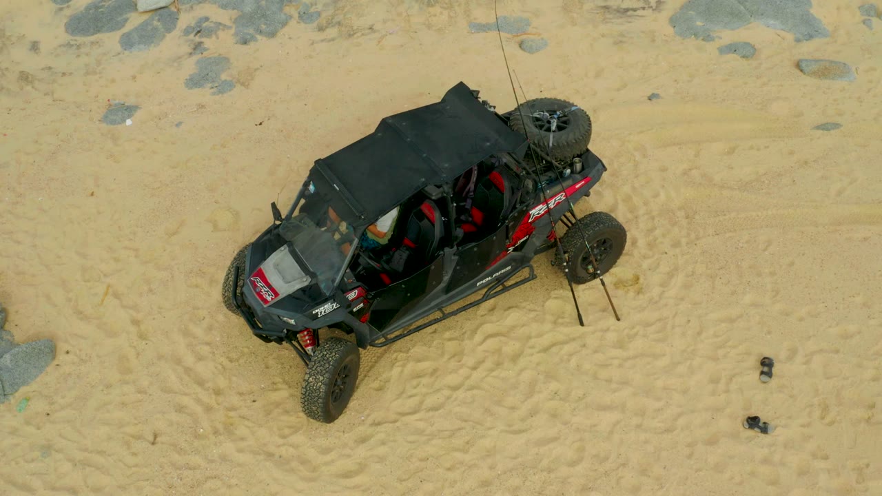 Overhead view of a black dune buggy with red accents on sandy beach terrain in Laguna Beach Los Cabos, Mexico, with rocks nearby and no clearly visible people.