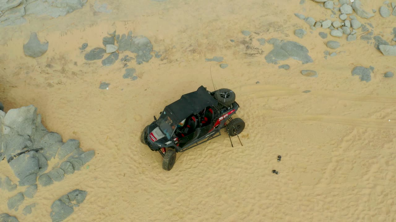 Black off-road vehicle crossing sandy terrain beside rocks.