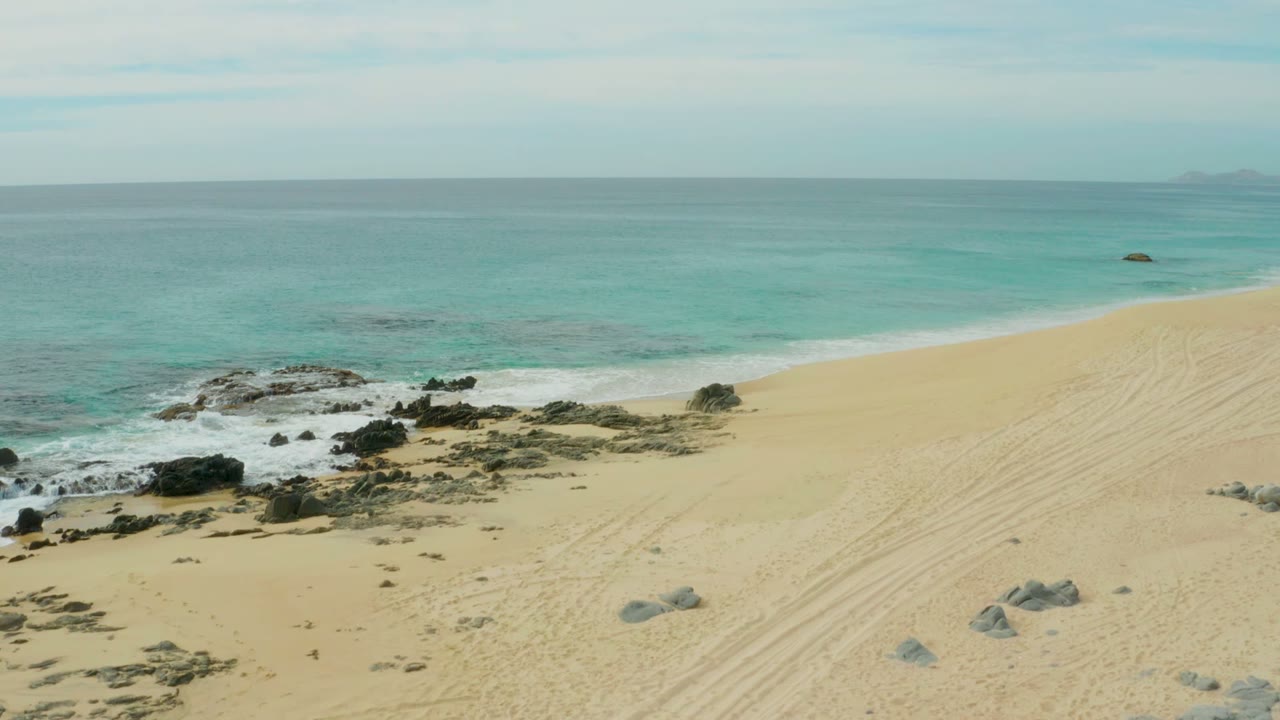 Rocky shoreline and turquoise water beside open sand.