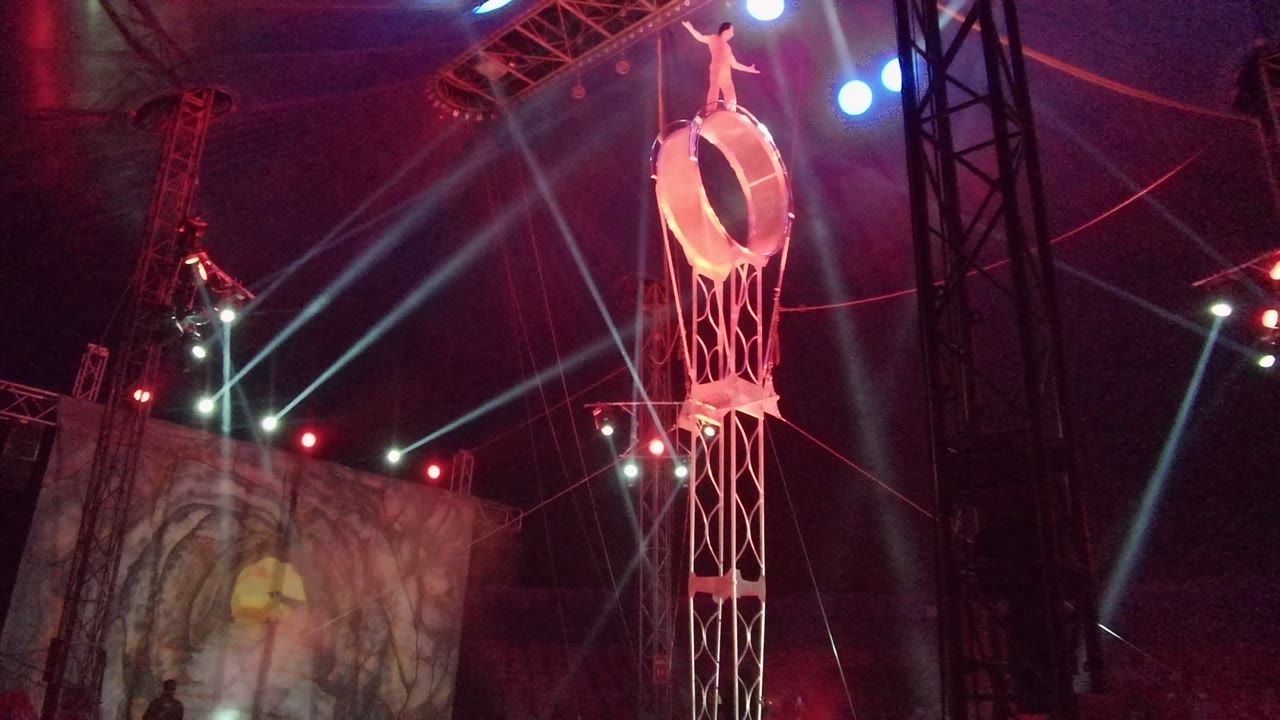 High ring performer above a stage with beams of light crossing the background.