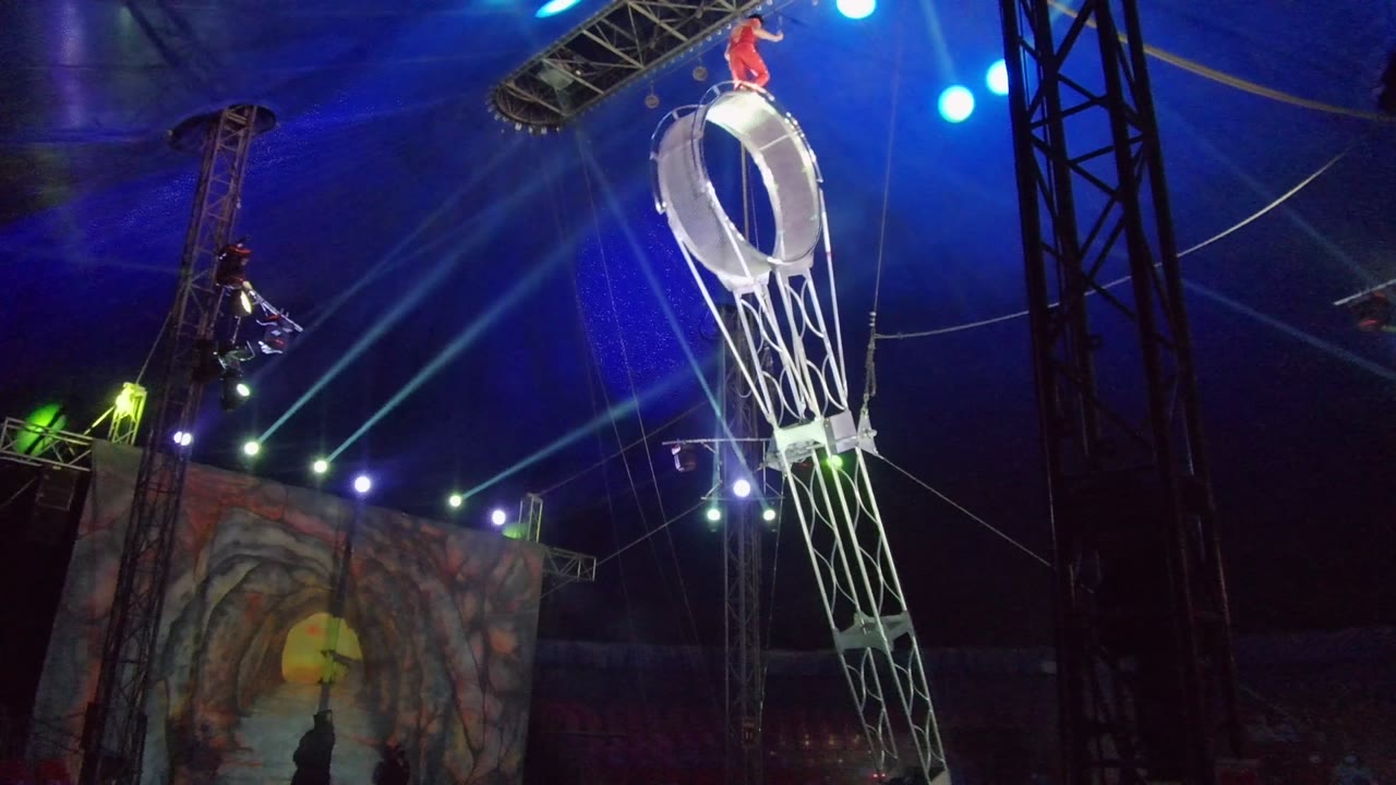 Aerial wheel tilted with a red-clad performer balancing on top.
