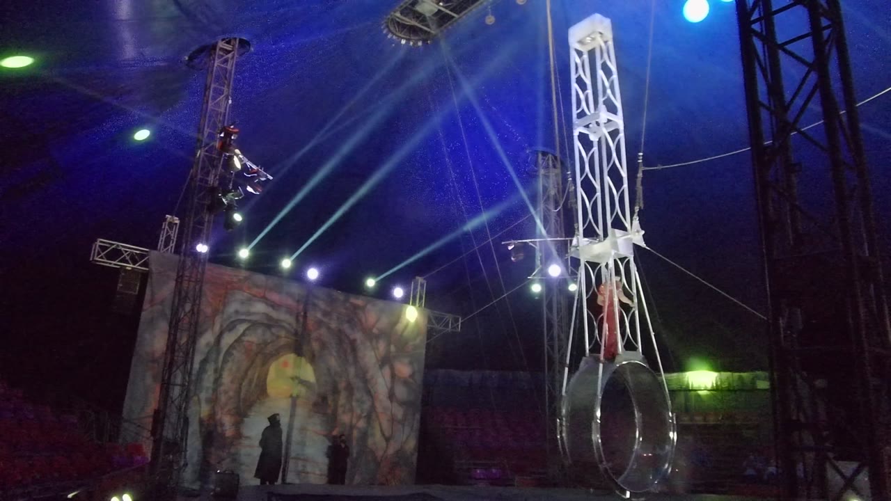 In San Jose del Cabo, the white truss has moved nearly vertical with the silver ring low in frame and the red performer partly visible against the stage rigging and blue lights.