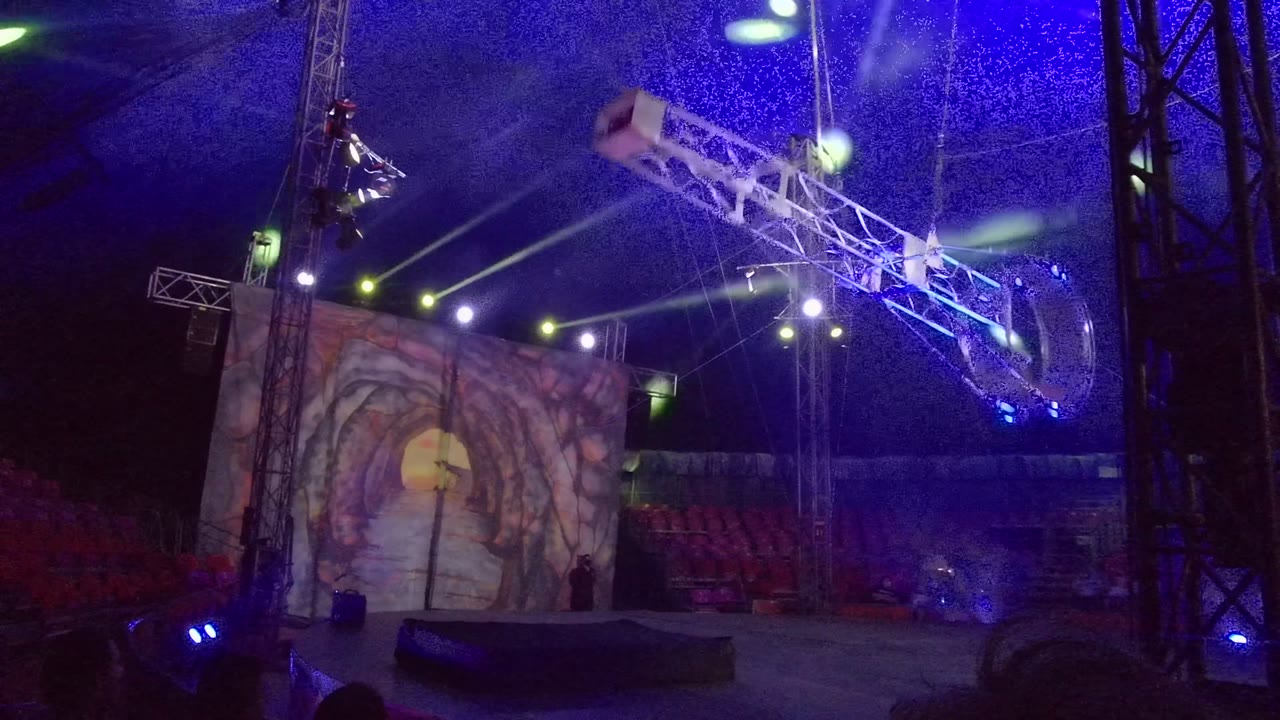 In San Jose del Cabo, the aerial apparatus angles across the upper right of the frame while blue and green stage lights cross above a scenic screen and rows of red seats.