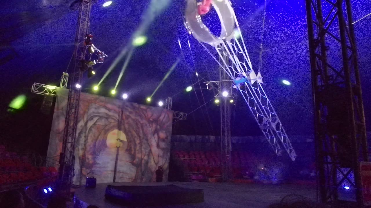 Suspended ring and metal arm move across a blue-lit performance tent.