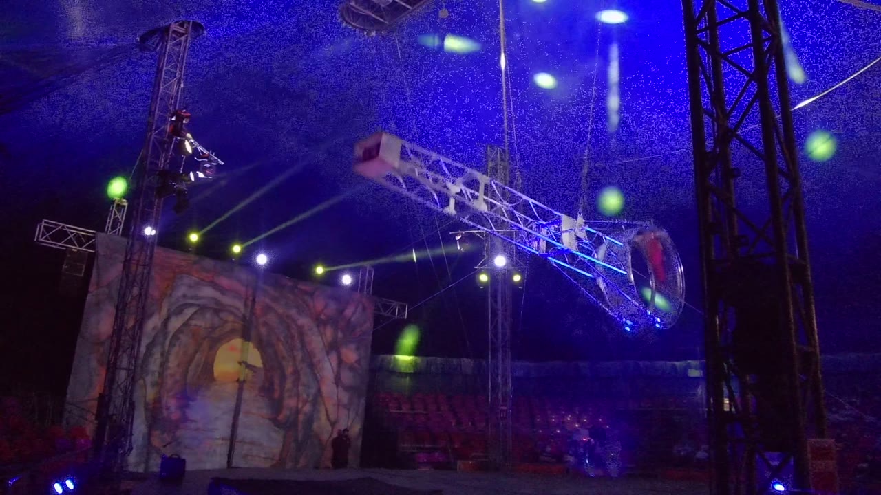 Rotating ring rig swings across the stage near aerial performers.