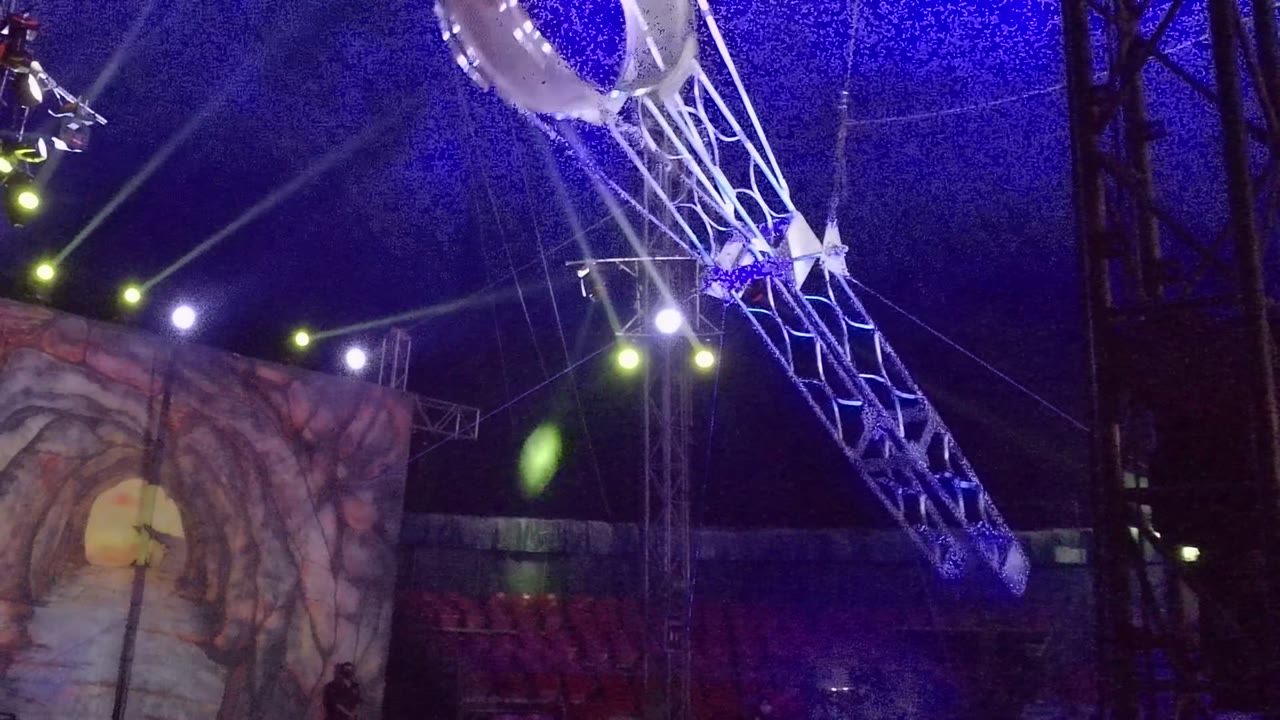 In San Jose del Cabo, a suspended hoop rig crosses the top of a blue-lit stage while a painted cave backdrop and rows of seats sit behind it.