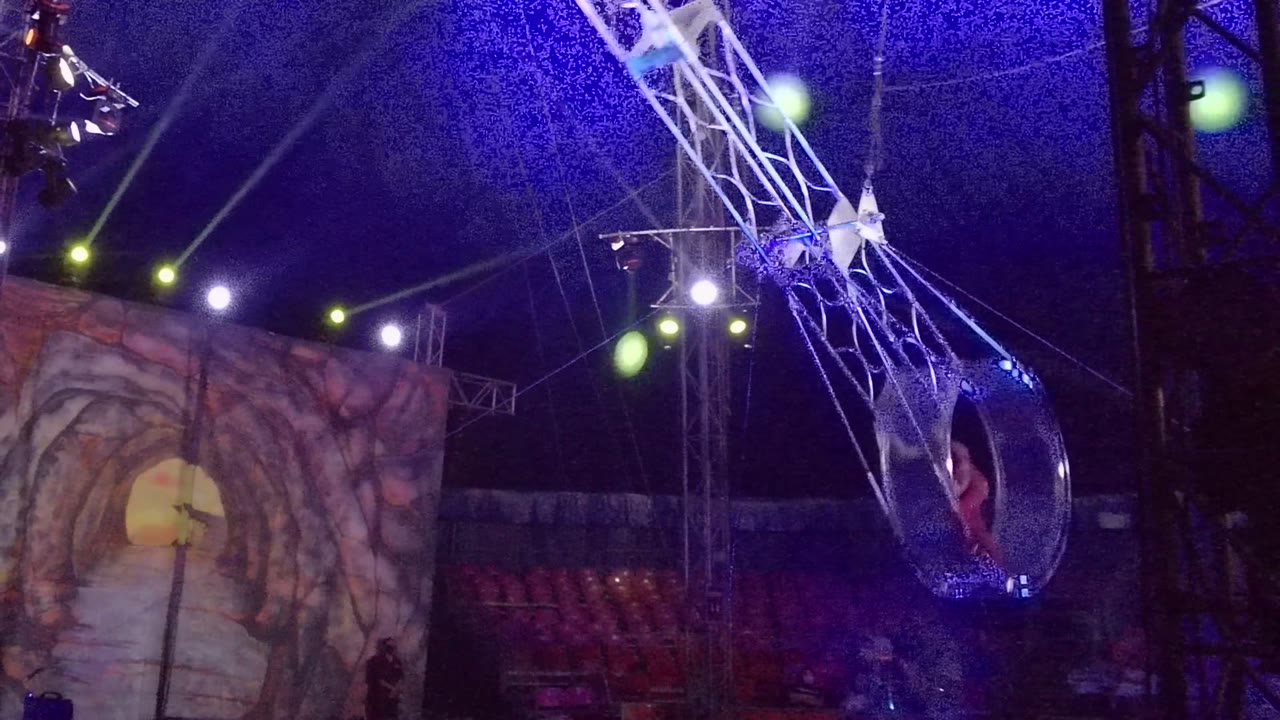 In San Jose del Cabo, the hoop moves toward the right side of the frame with the red performer partly visible against dark rigging and blue overhead light.