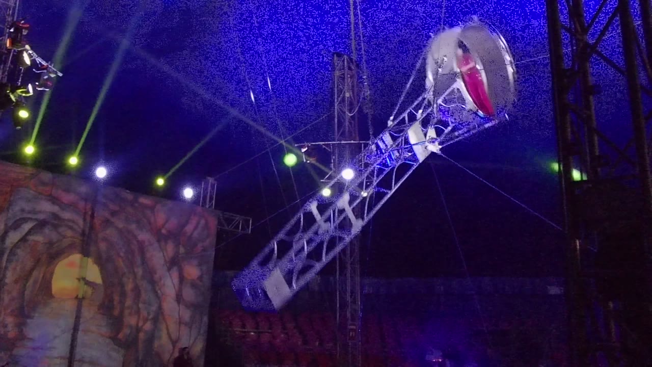 Mechanical arm lifts a circular cage near stage lights.