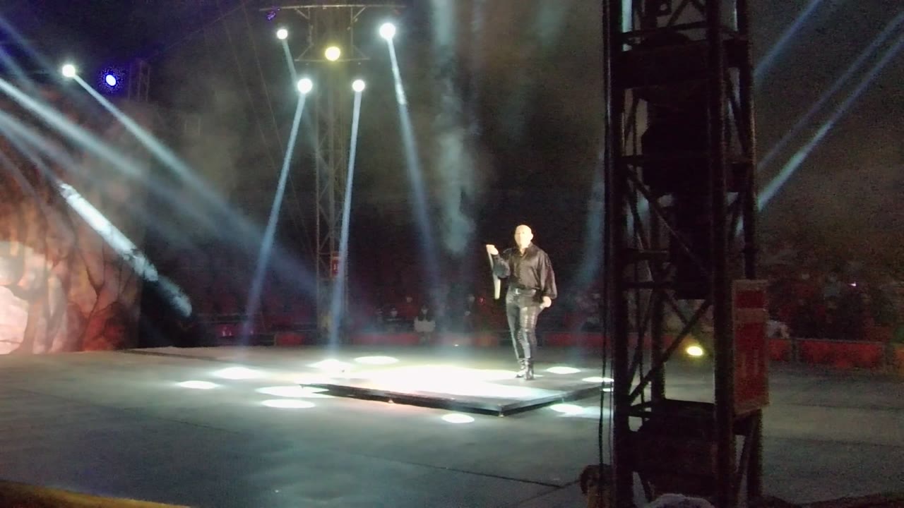 Performer on a bright stage with spotlights and a staff nearby.