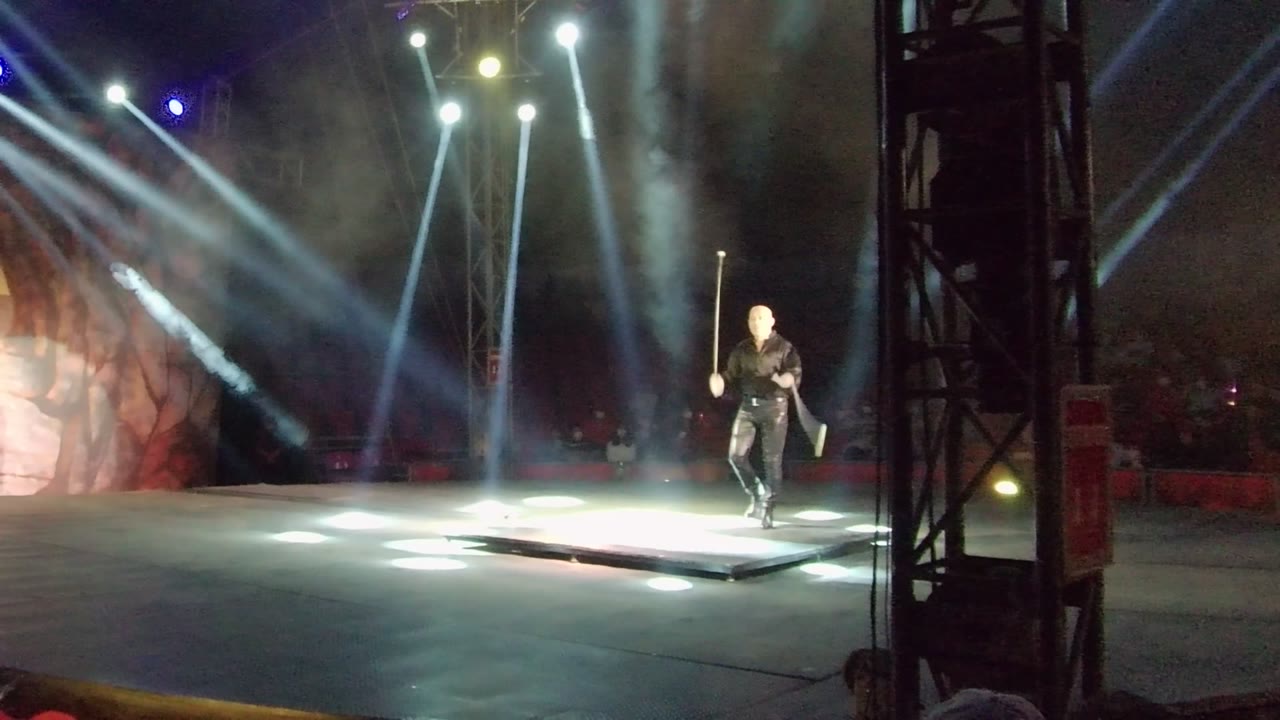 The performer in San Jose Del Cabo moves across the bright stage area with the staff raised upright, while overhead lights create white pools on the floor.