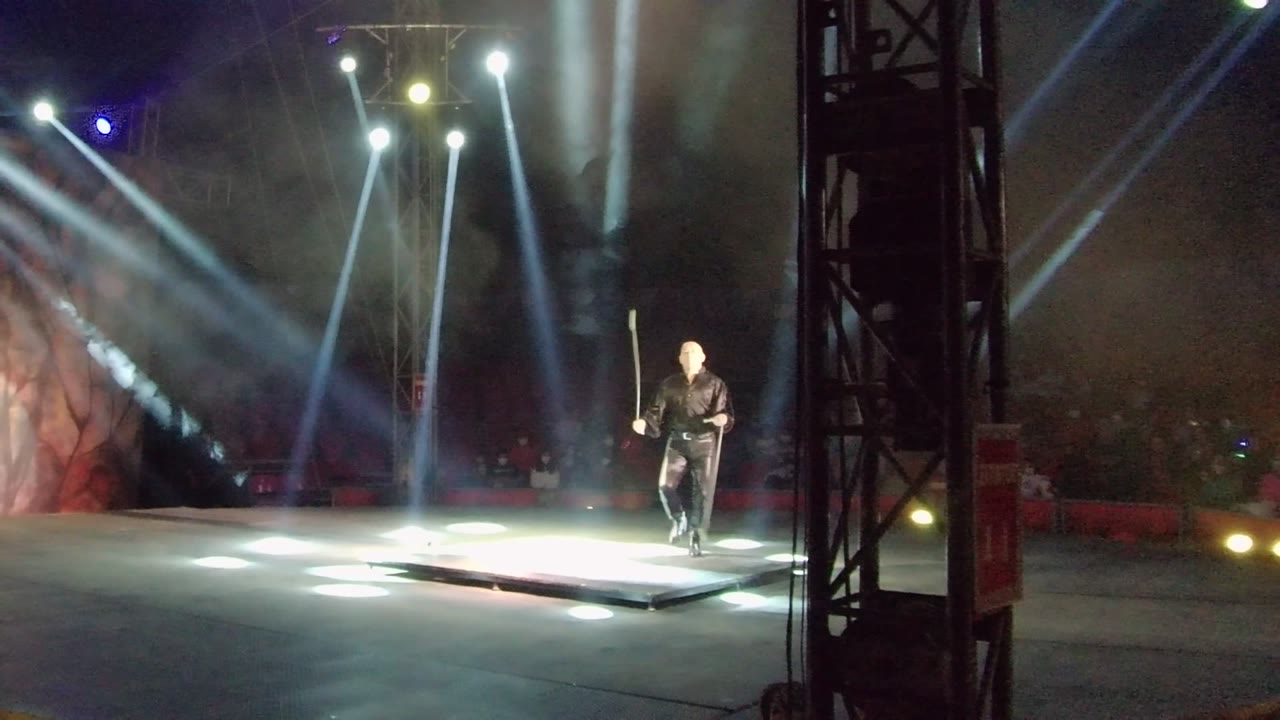 Performer twirls a staff near the edge of a lit stage.
