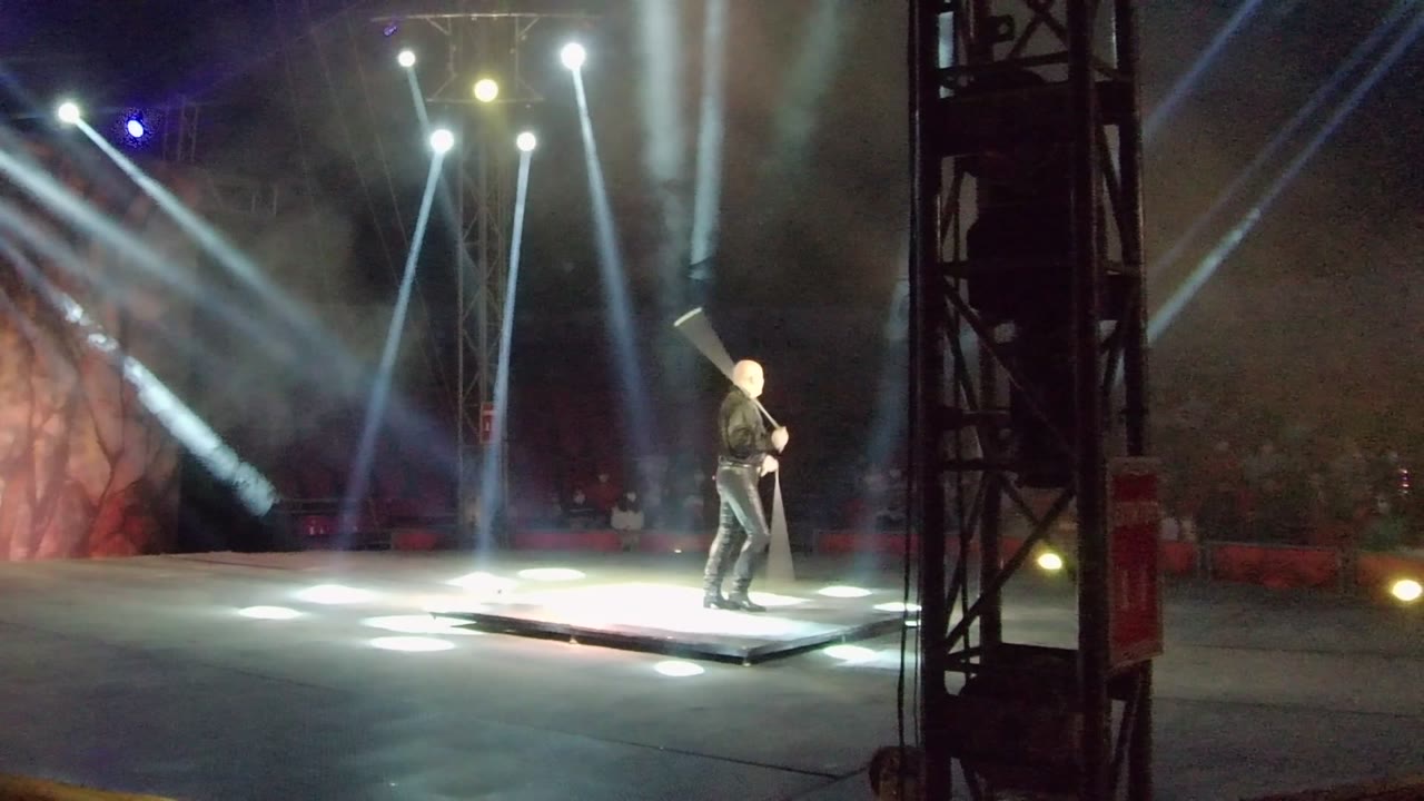 In San Jose del Cabo, Mexico, the performer reaches the right side of the illuminated stage while pale spotlights cross the smoky dark backdrop.