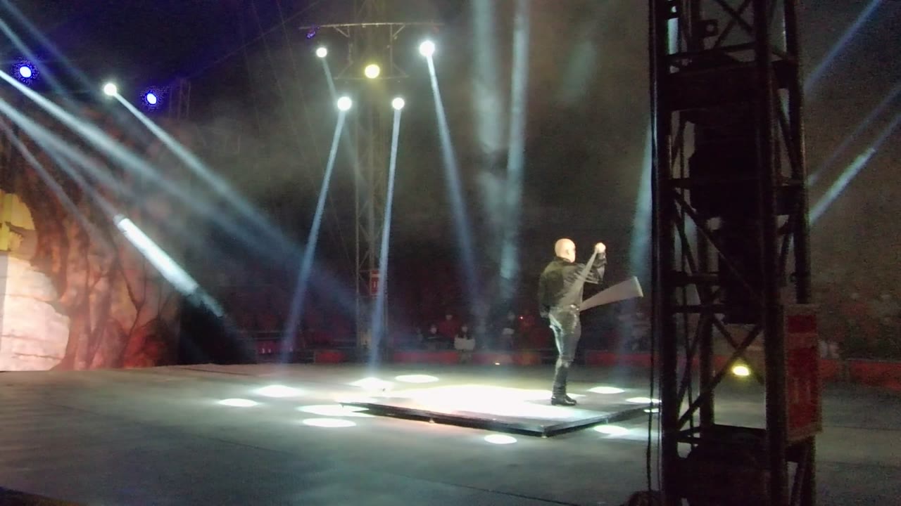 Performer holding an axe beside bright floor spotlights.