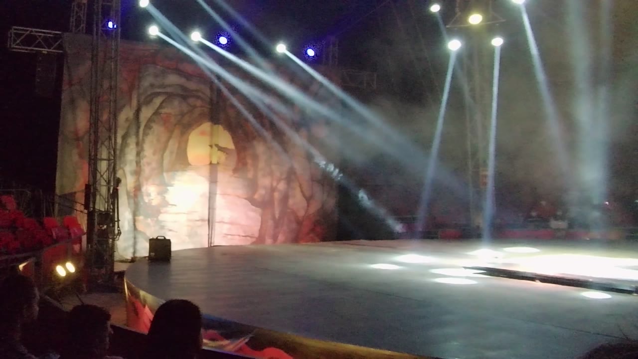 The stage in San Jose del Cabo is nearly empty as the performer reaches the right side, leaving white spotlight pools and smoky beams over the main floor.