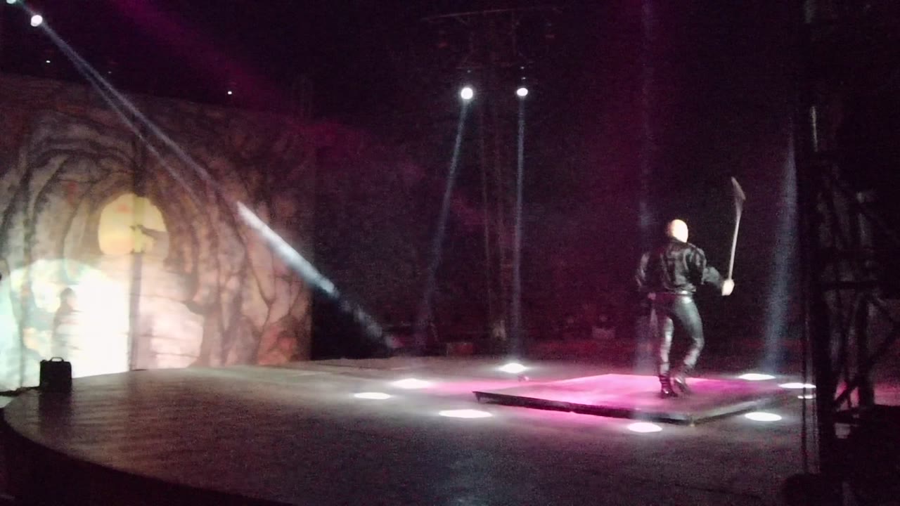 Performer walks across stage holding a long prop.