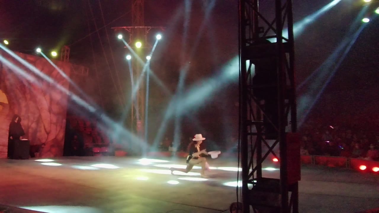 The solo dancer drops into a low pose on the San Jose del Cabo stage as white beams fan overhead and red light washes the backdrop.
